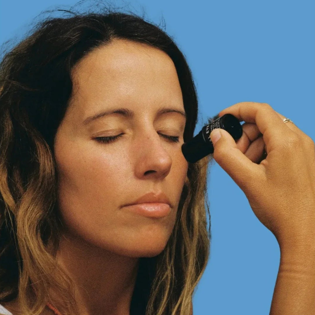 Woman applying Eye Balm against a blue background