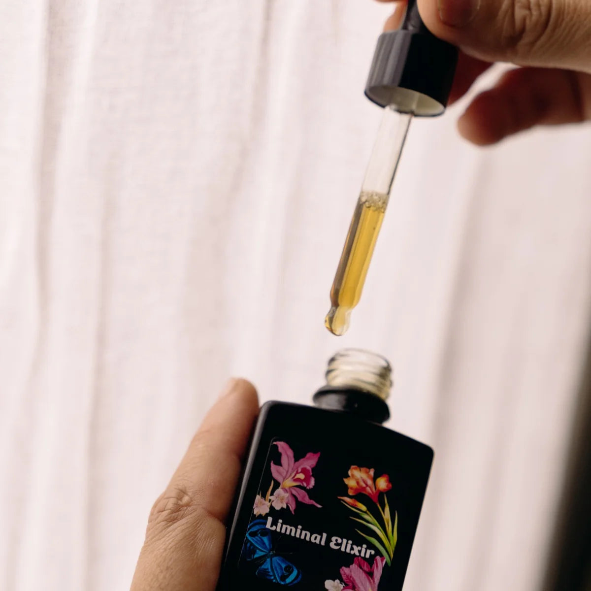 Hand holding a dropper with liquid above a bottle labeled &