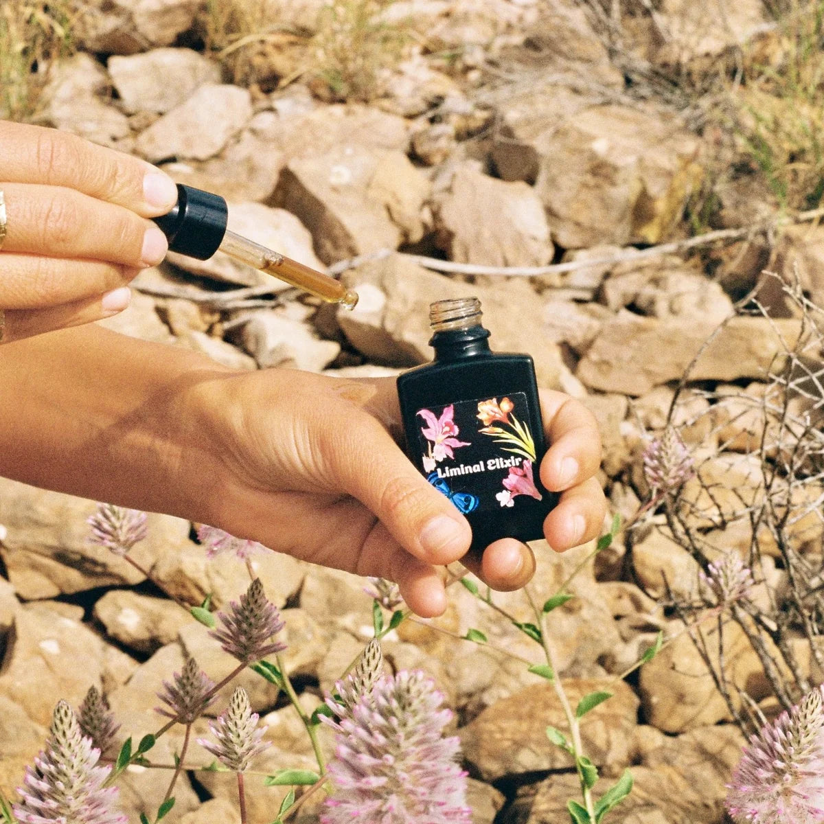 Hand holding a small bottle with a dropper against a rocky background