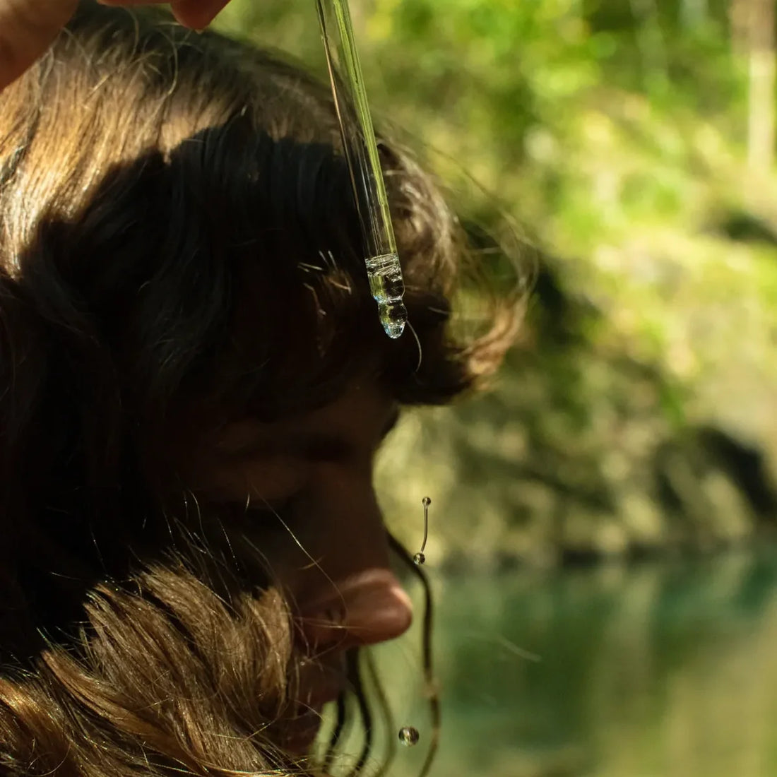 Woman using dropper to apply hair oil outdoors.