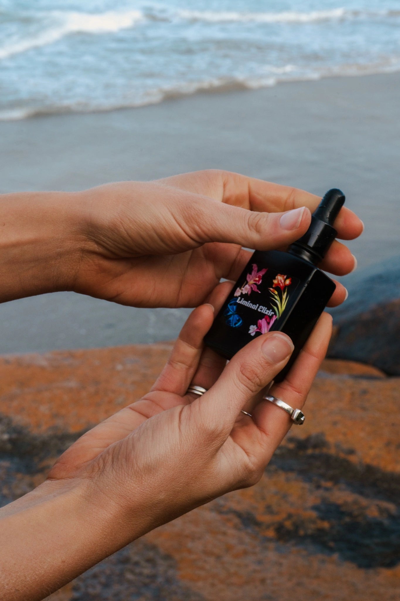 Hand holding a small black bottle with floral design on a beach
