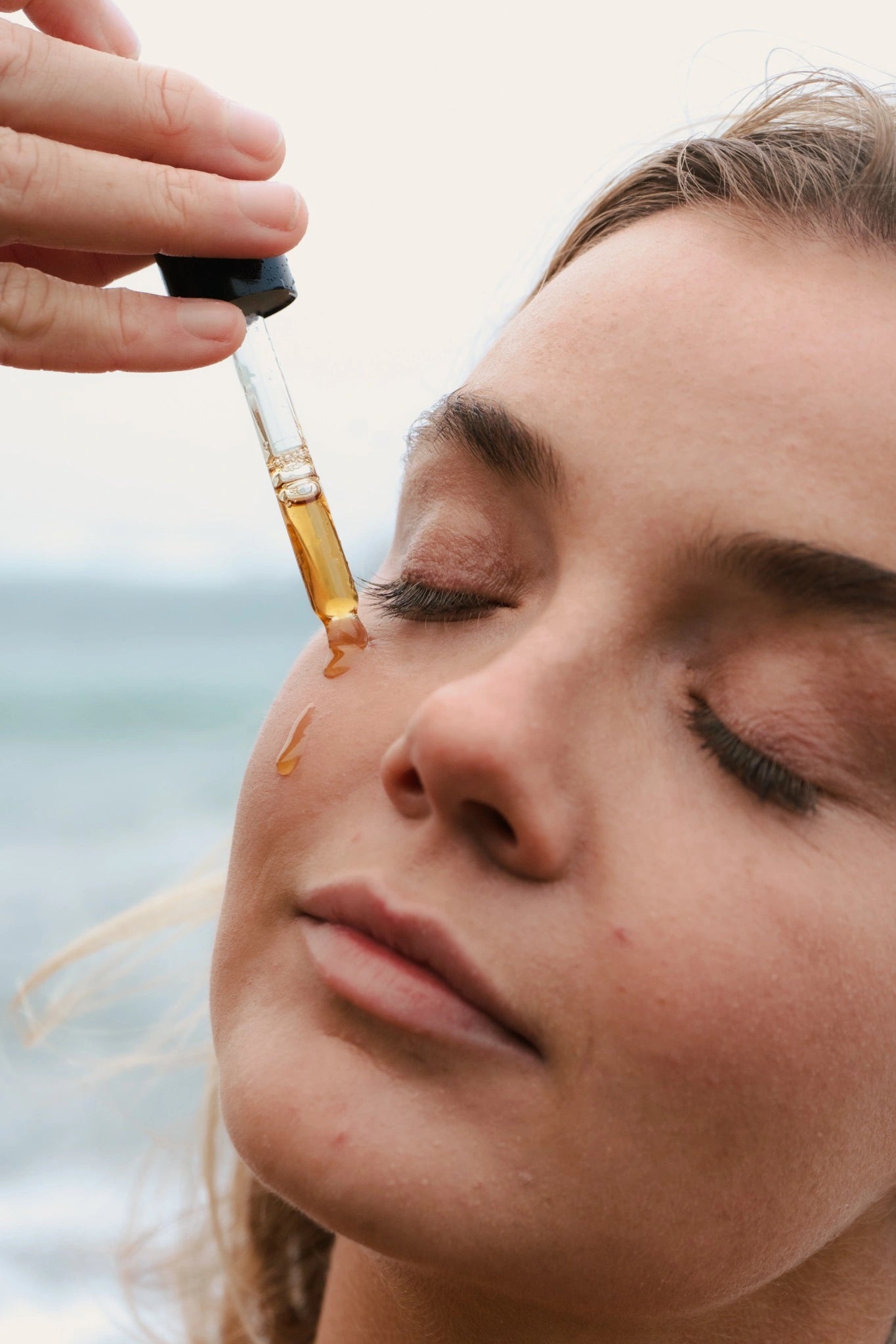 Person applying a dropper of oil to their face with a blurred background
