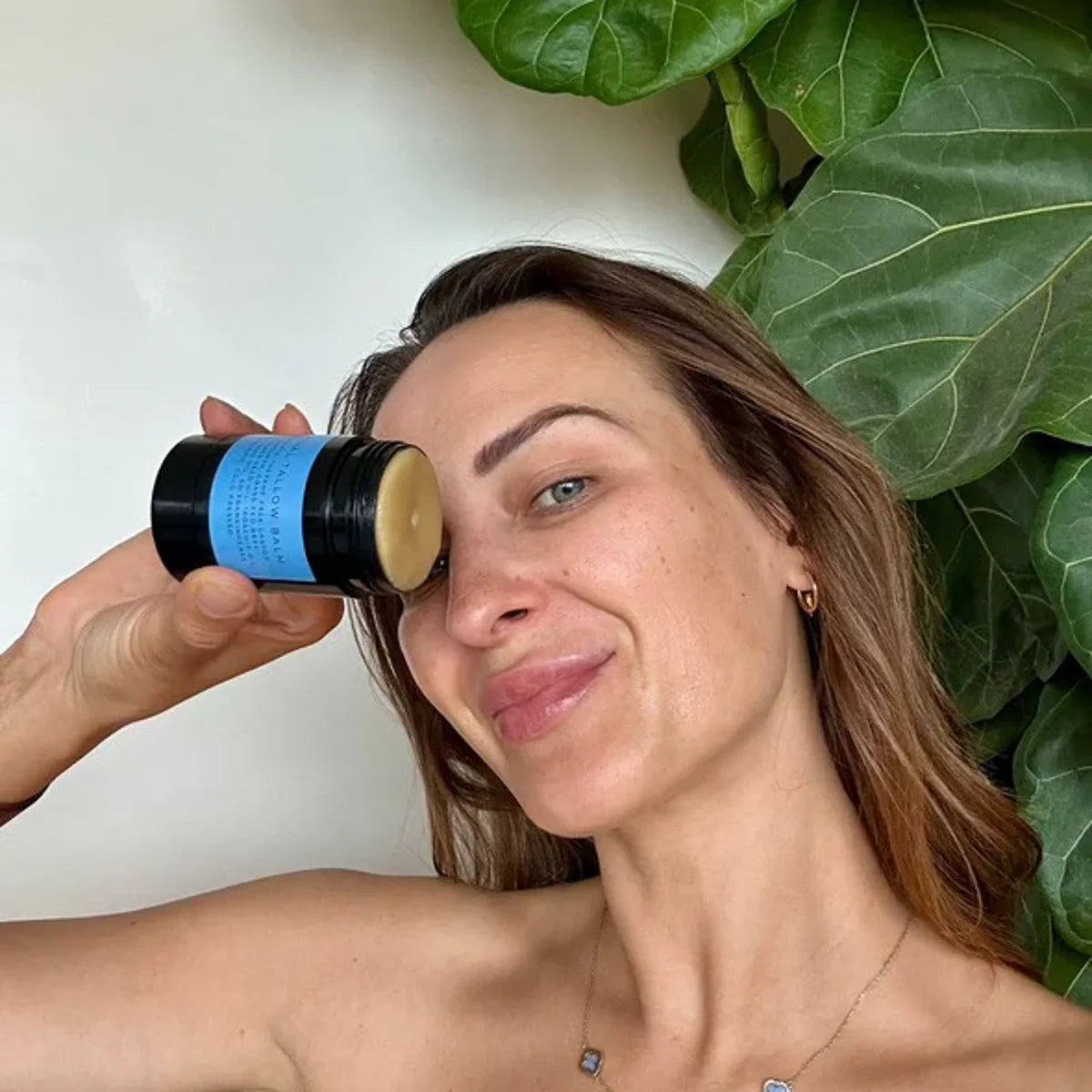 lady smiling and holding tallow balm stick near face