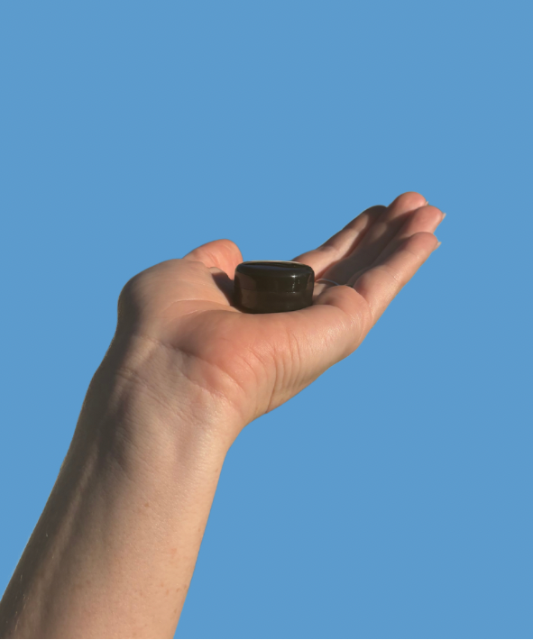Hand holding a small longveity balm sample against a blue background