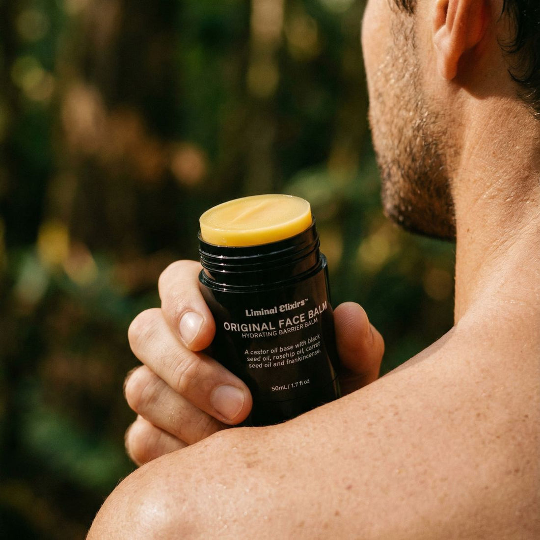 Man holding a black Liminal Man face balm container with balm showing outdoors