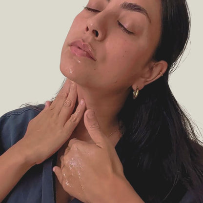 Woman applying Liminal Cleansing Elixir Oil skincare product to their  face and neck with a neutral background