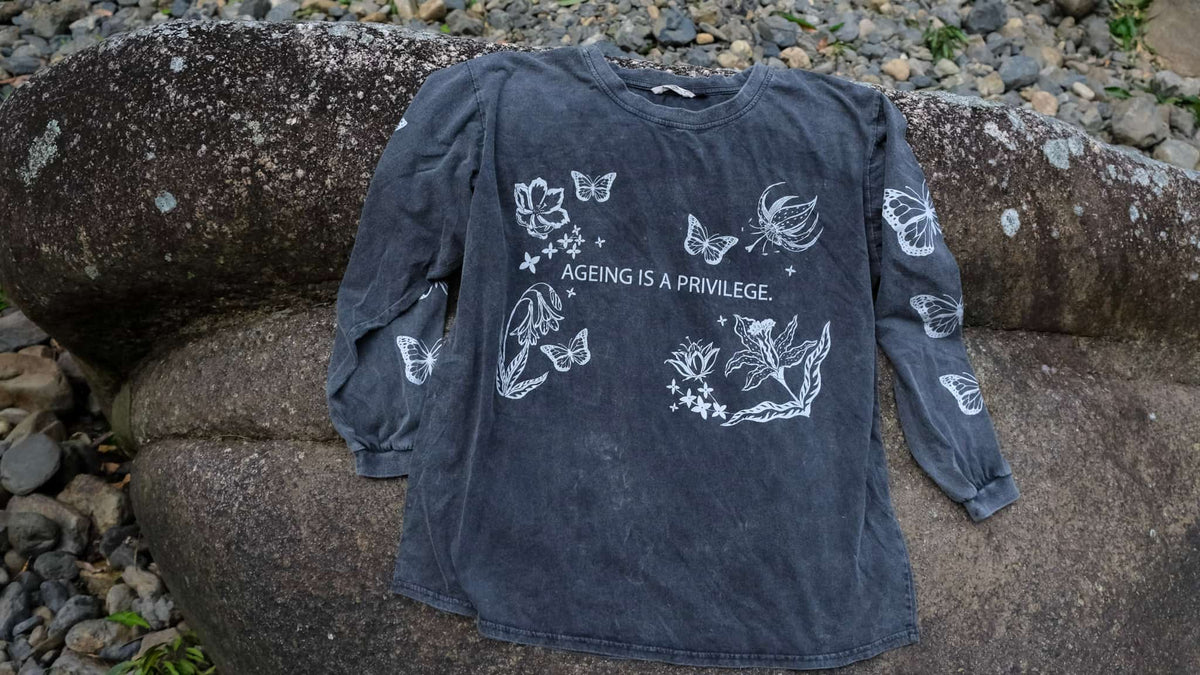 A dark washed charcoal long-sleeve t-shirt with white butterfly and floral illustrations and the text &