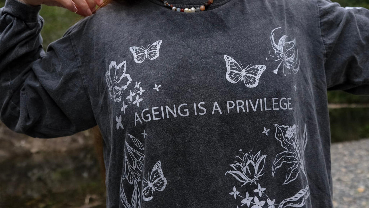 A person wearing a dark gray long-sleeve t-shirt with white line art illustrations of butterflies, lotus flowers, and the text &