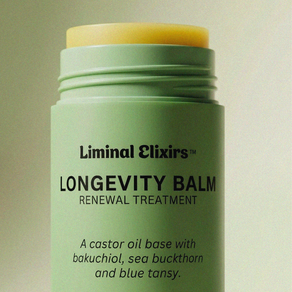 Green longevity balm with yellow cap on a beige background
