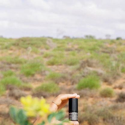 Hand holding Eye Balm with bushes in background