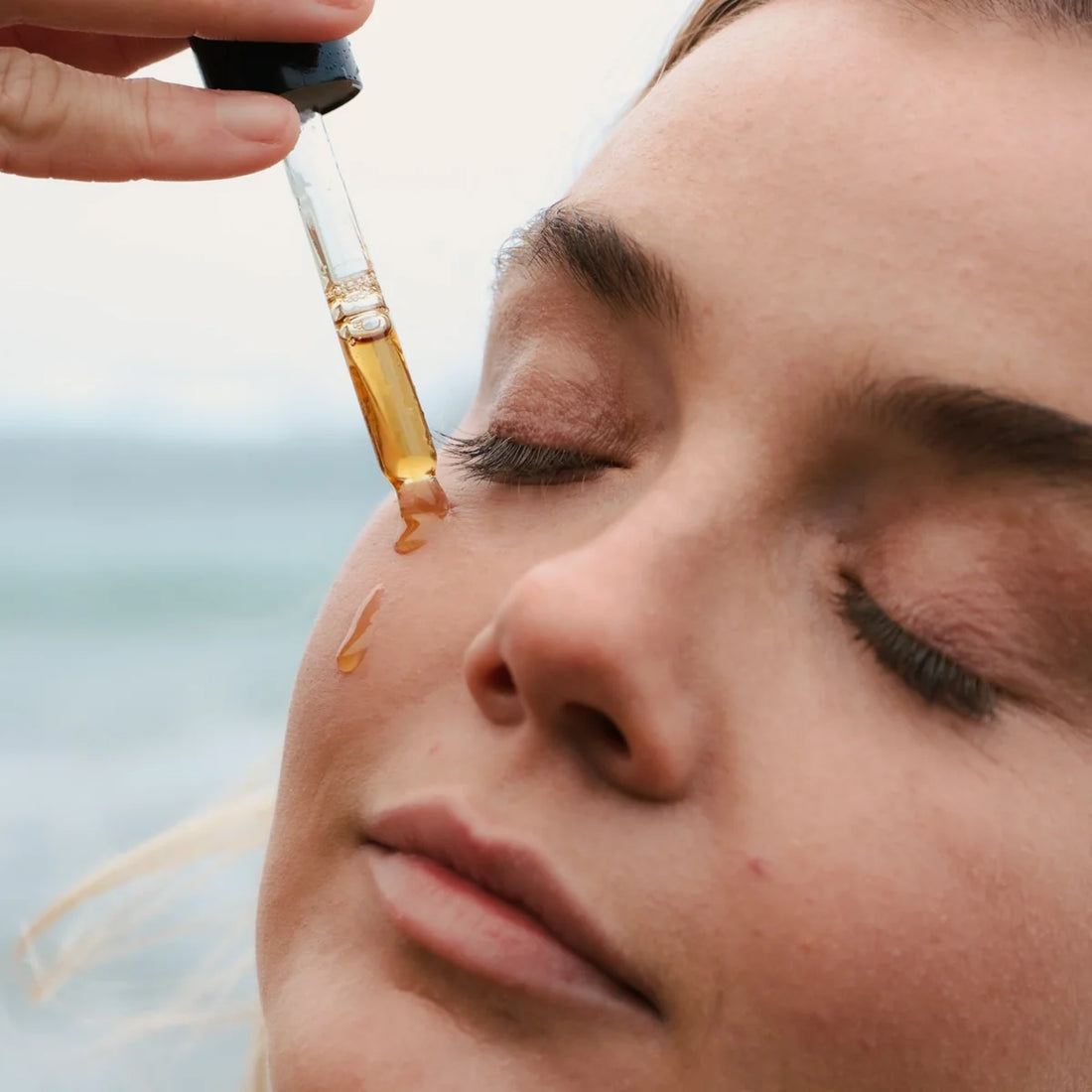 Close-up of a woman applying a dropper of oil to her skin with a blurred background