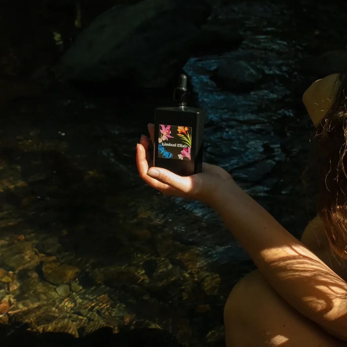Hand holding scalp oil bottle near river.
