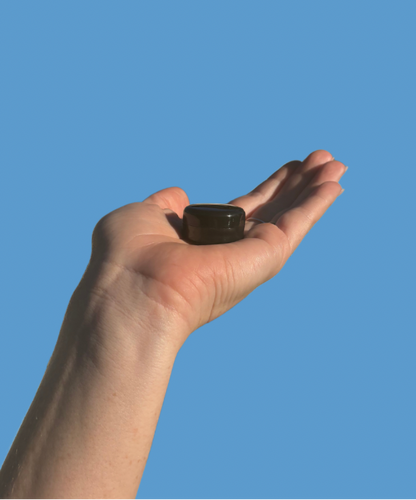 Hand holding a small longveity balm sample against a blue background