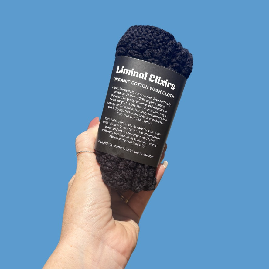 Hand holding a black organic cotton wash cloth with &